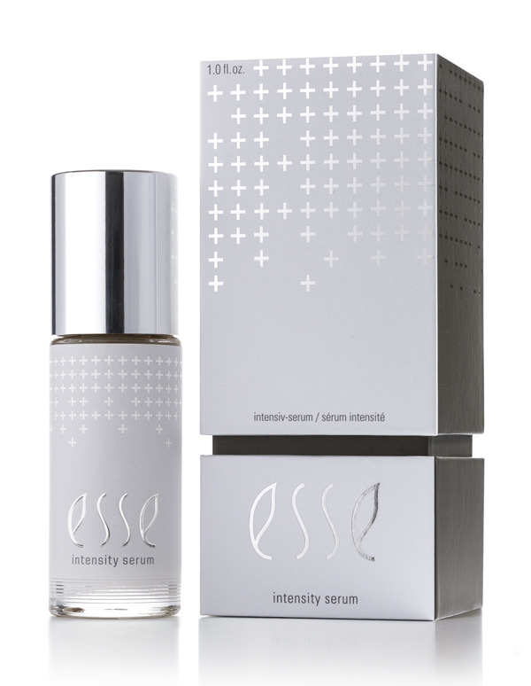 The Esse Intensity Serum, featuring a shiny silver cap and the Esse logo, stands beside its matching silver and white box decorated with small crosses.