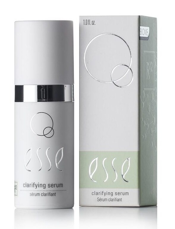 A 1.01 fl. oz. bottle of Esse Clarifying Serum is displayed alongside its packaging. The bottle, which is white with a silver cap, bears a label adorned with elegant circular designs. The packaging mirrors the design of the bottle and includes additional informational text.