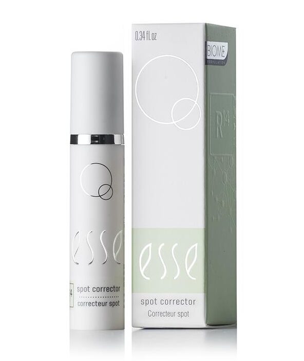 A compact, white bottle of Esse Spot Corrector is showcased beside its coordinating box. Both the bottle and the box boast minimalist designs, adorned with the brand name "esse" in an elegant, lowercase script and circular geometric elements. The box also includes additional text and a light green panel.