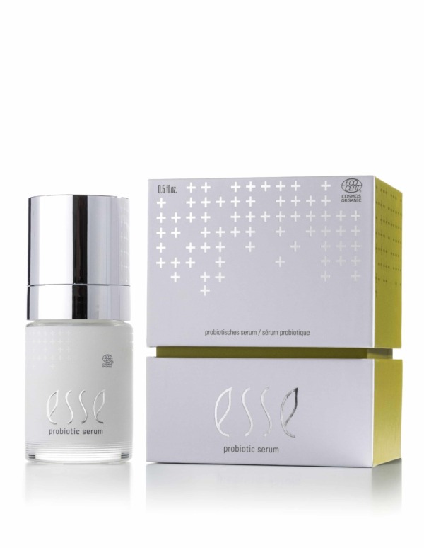 The Esse Probiotic Serum is displayed with a silver cap beside its matching white and yellow box, which features a minimalist design with plus sign patterns.
